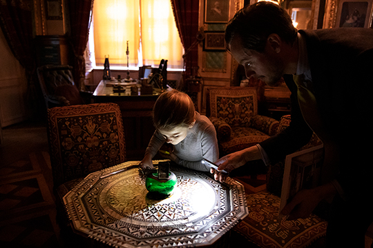 Prinsessan Estelle och intendent Alexander Holm tittar på ett bord i orientalisk stil som ursprungligen var placerat i Oskar II:s orientaliska rum på Stockholms slott. 