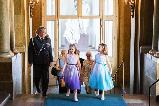 Emilia och hennes syster Maja blir eskorterade uppför Kungliga slottets östra trappa av Kronprinsessans adjutant. 