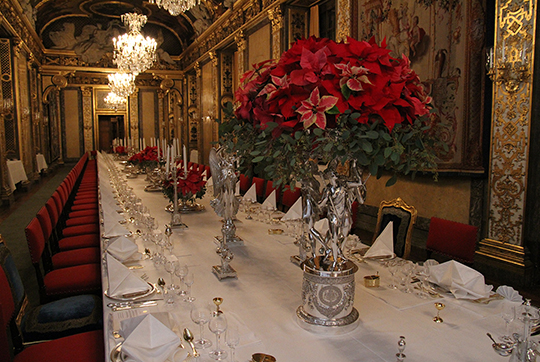 Bordet står klart för kvällens middag i Karl XI:s galleri. Blomsterdekorationerna består av julstjärnor och eucalyptus. Taffelsilvret, det vill säga de dekorativa silverpjäserna, är hämtade från den Brasilianska silverservisen. Bordet dukas med Fatburens äldsta linne, Unionslinne. Det är vävt år 1891 i staden Lille i Frankrike. 