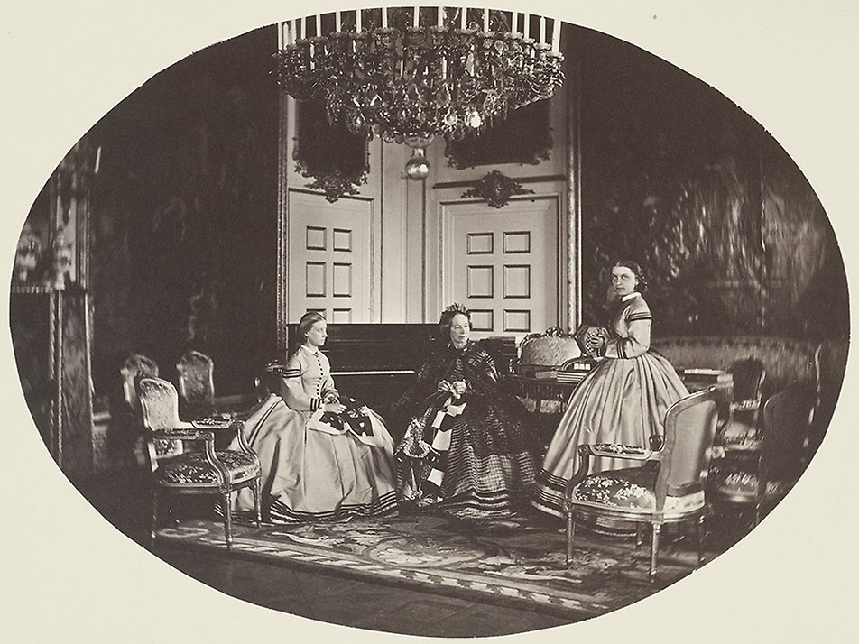 Änkedrottning Josefina i Ehrenstrahlsalongen på Drottningholms slott. Till vänster hovfröken Charlotte Lagerheim och till höger, med dragspelet, hovfröken Lotten von Heijne. Bilden är från 1860-talet.